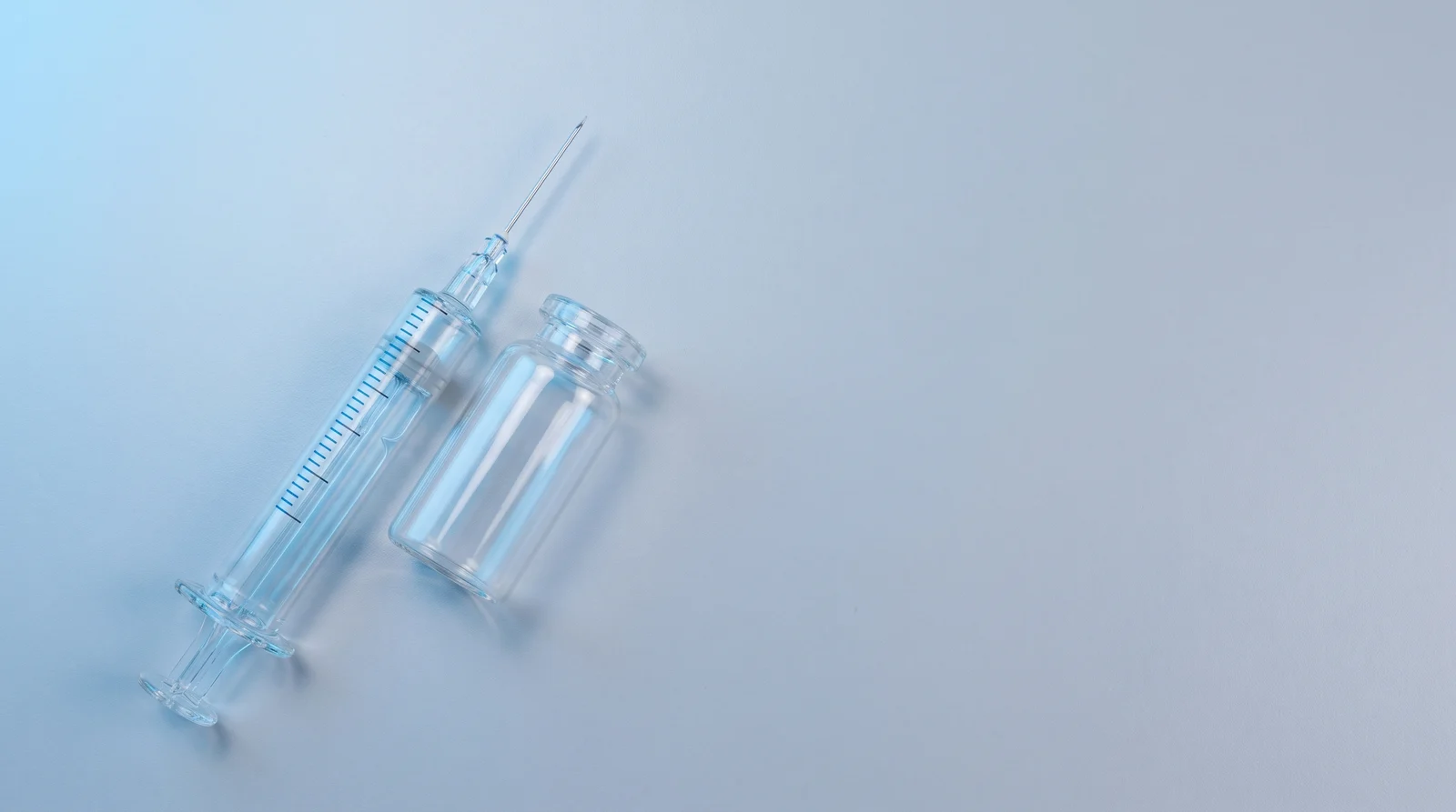 An empty syringe beside an unmarked vial on a clean surface, with no packaging or instructions.